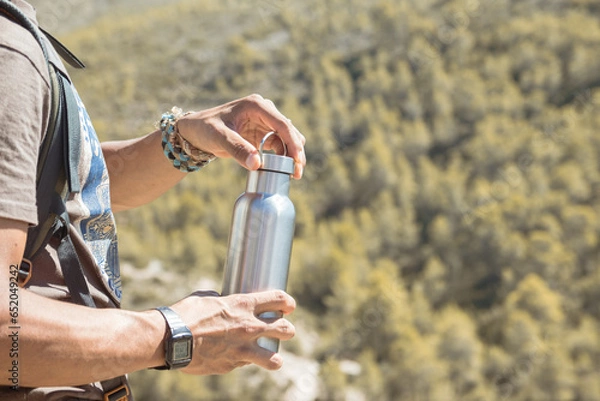 Obraz Hand taking an aluminum thermal bottle to hydrate on a hiking trail