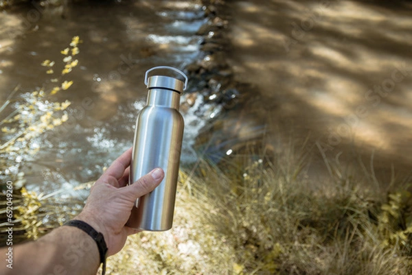 Obraz Hand taking an aluminum thermal bottle to hydrate on a hiking trail