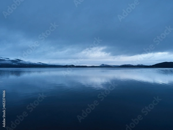 Fototapeta View of a lake in a winter blue hour in the evening. The water makes a mirror effect to the sky