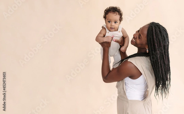 Fototapeta African-American mother with baby smiles and rejoices on beige background Minimalist portraits, space for text
