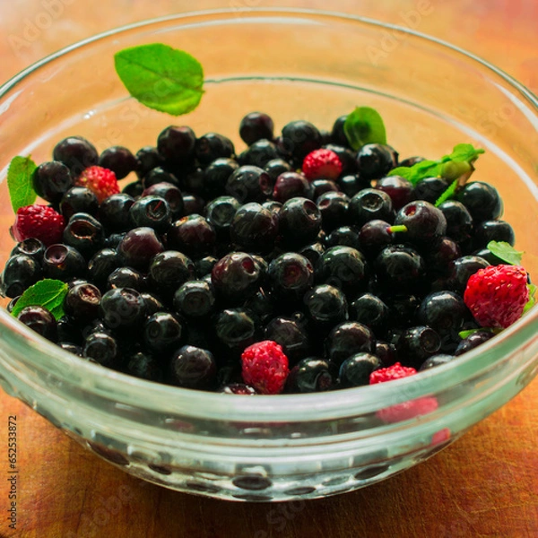Fototapeta Red and black berries in a glass dish on a wooden background.