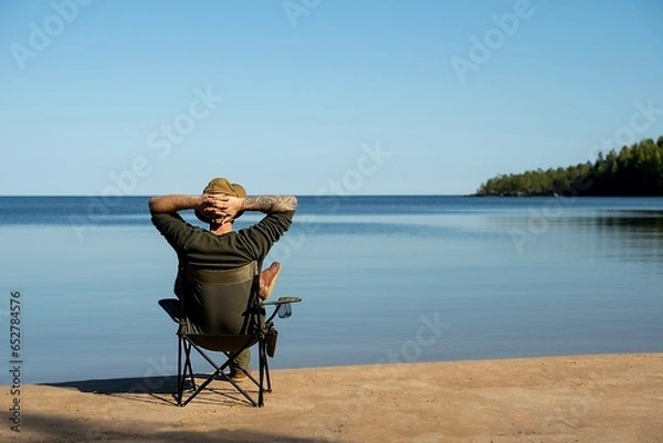Obraz Man rests on a camping chair and looks out over the lake on a sunny day