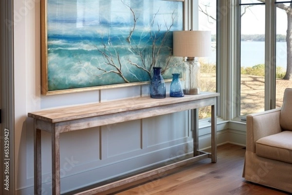 Fototapeta window view of a sea landscape painting hung above a weathered oak console table