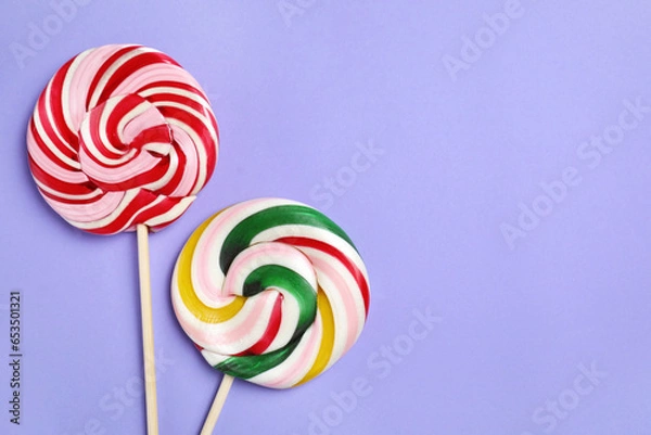 Fototapeta Sticks with colorful lollipops on violet background, flat lay. Space for text