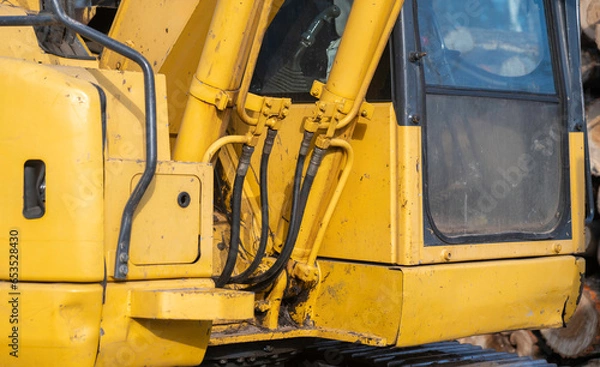 Obraz Closeup detail of a working, used, dirty yellow excavator, centered on hydraulics hoses and pipes next to the window of the operator cab.