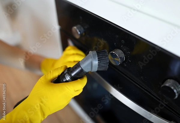 Fototapeta Close-up of male hands in yellow gloves vacuuming cookstove handle with special vacuum cleaner after setting. New modern cooker. Renovation and furniture change concept