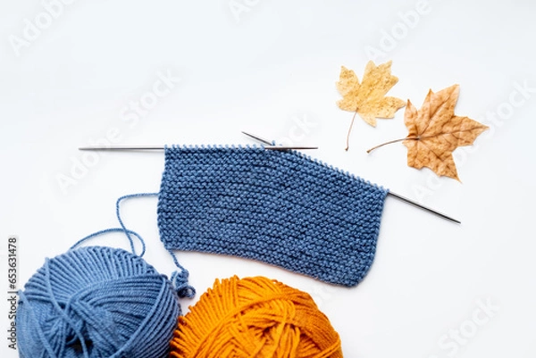 Obraz A piece of cloth knitted with blue threads and two balls of blue and yellow threads on a white background 