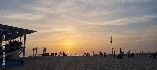 Fototapeta Sunset on the beach with silhouettes of people enjoying the view.