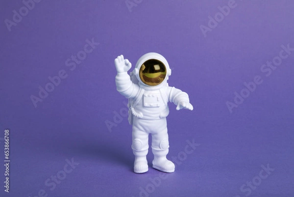 Fototapeta an astronaut figurine in a spacesuit exploring a plain purple background