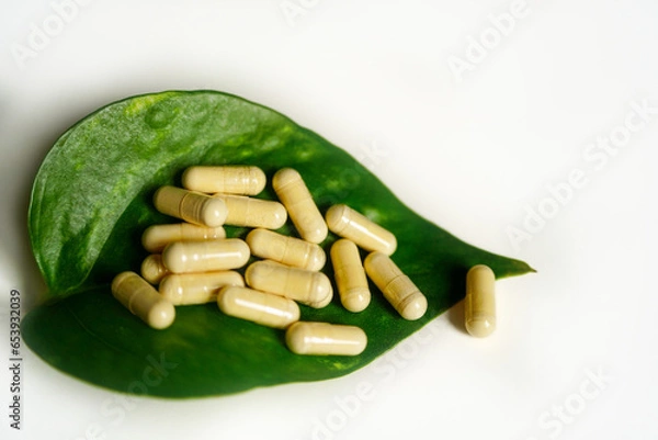 Obraz Vitamin D capsules on a green leaf with white background.