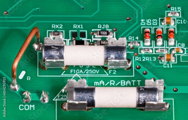 Fototapeta Closeup of ceramic tubes of electrical fuses in metal holder on circuit board. Low ohm wire resistor to current measuring, capacitors or red diodes. Surface mounted electronic components on green PCB.