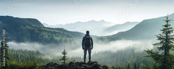 Obraz A lonely man enjoys the view of the summer mountains while he standing on a mountain peak. Hiking and digital detox concept. Contemplation of nature alone with your thoughts. Format photo 5:2.