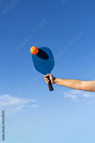 Fototapeta Arm with blue paddle hitting orange pickleball ball
