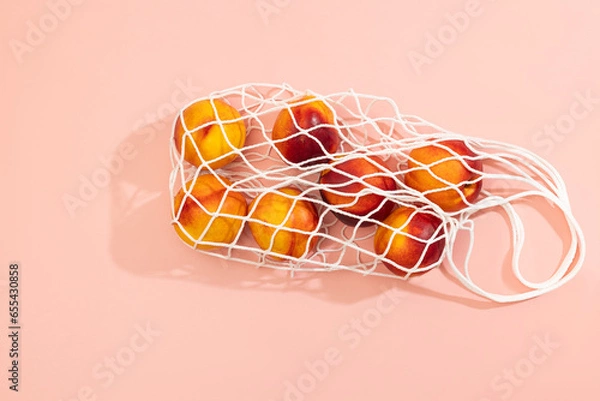 Fototapeta Nectarines in a white string bag on a pink background