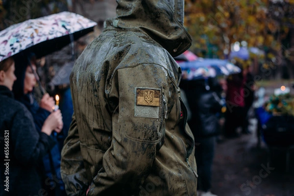 Fototapeta A Ukrainian serviceman in the rain at the funeral of his comrade who died during Russia's invasion of Ukraine. Dramatic background, cold colors. Concept of war and peace