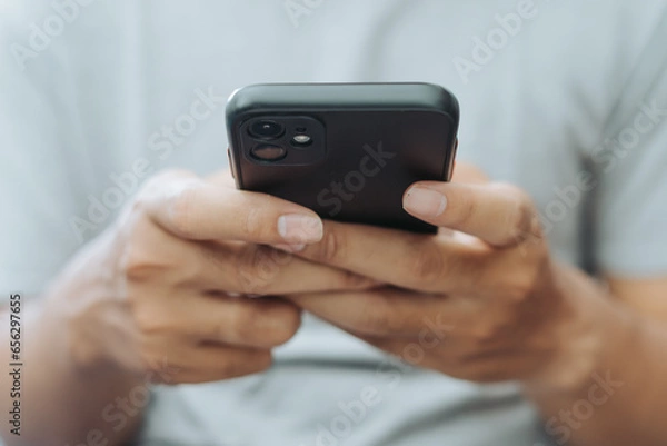 Fototapeta Hands of Asian man holding checking touching scrolling smartphone from bed room