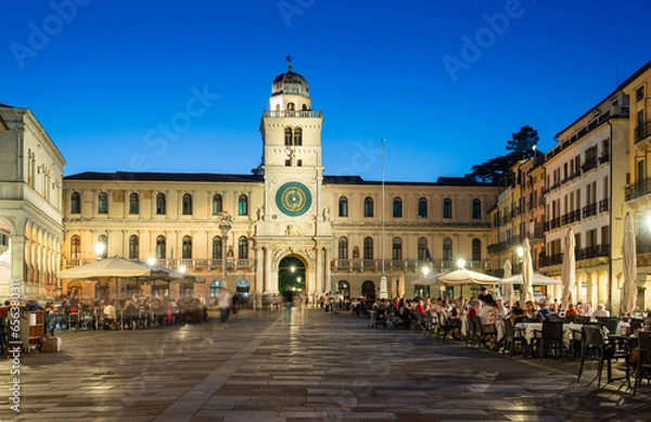 Fototapeta Padua, Italy - October 1, 2023: Piazza dei Signori or Piazza della Signoria in the evening. The square is dominated by the famous Clock Tower. People sitting at the tables in the bar or walking around