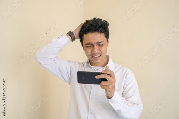 Obraz Indonesian office employee wear white clothes unhappy playing game when working hour. The photo is suitable to use for man expression advertising and fashion life style.