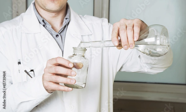 Fototapeta Laboratory assistant pours liquid from a flask