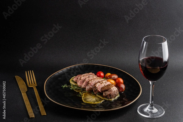 Obraz Roasted duck breast fillet on caramelized apples. the dish lies on a black plate on a black background. glass of red wine
