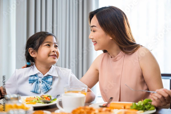 Obraz Asian family breakfast. smiling mother and child daughter having breakfast on food table, Healthy food at home before go to school, Mom and little preschooler have fun eating meal together