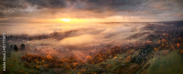 Fototapeta Highly dramatic sunrise scenery from above the fog. Panoramic aerial view of a beautiful landscape with magnificent red light illuminating dark clouds and the mist