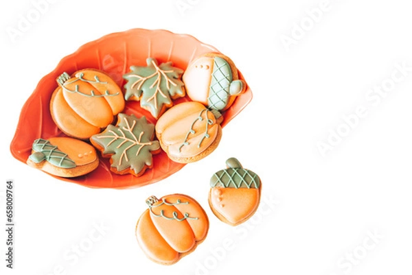 Obraz Gingerbread cookies in the shape of a pumpkin, acorn and maple leaf with multi-colored glaze in an orange plate on the kitchen table. Delicious cookies for children's holidays.