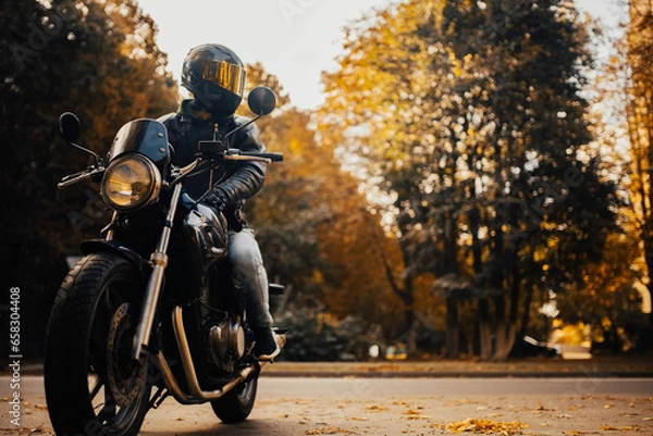 Fototapeta motorcyclist in a helmet with a classic motorcycle in the fall. Stylish motorcyclist in a leather jacket and gloves.