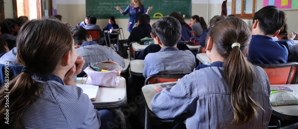 Fototapeta Group of students in a classroom with a teacher explaining a topic.  Boys at their desks dressed in uniform. Education. Children learning at school.
