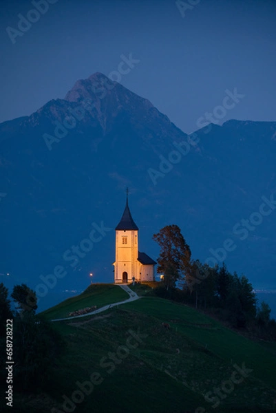 Fototapeta Illuminated The Church of St. Primoz and Felicijan in the village of Jamnik in the Slovenian Alps at night. Vertical view