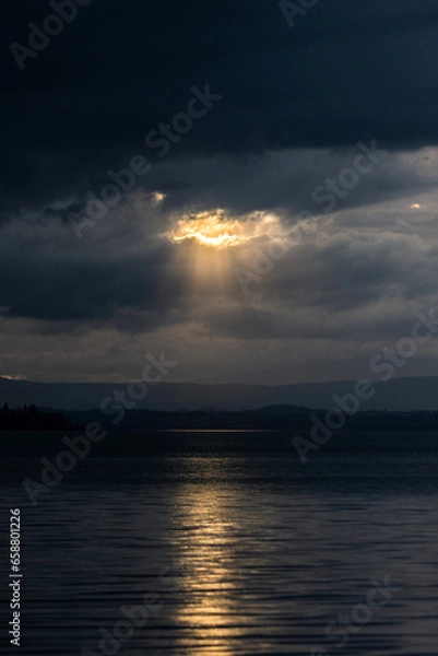 Fototapeta Sunset on Trasimeno lake in Umbria, Italy, with the sun coming down behind moody clouds and beautiful water reflections