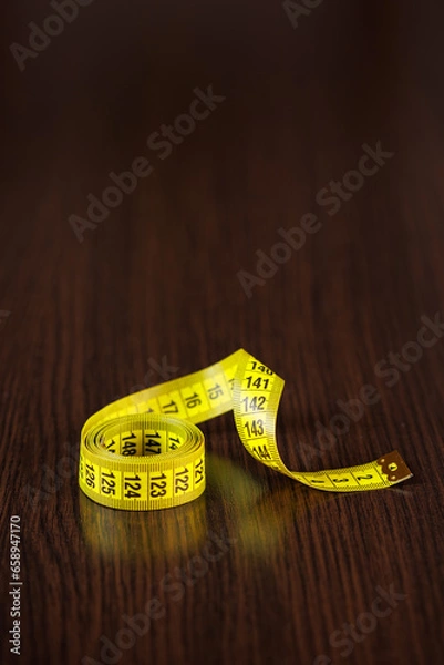 Fototapeta A tailor's measuring tape of yellow color lies on a dark wooden table. Selective voicing. Place for text. Copyspace.