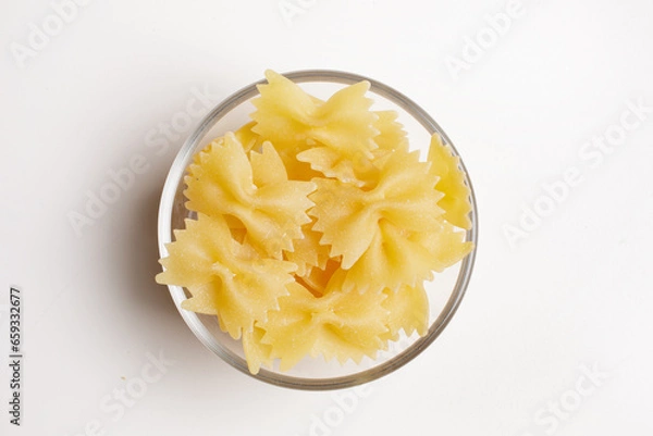 Fototapeta Durum wheat farfalle macaroni in a glass bowl on a white background seen from above