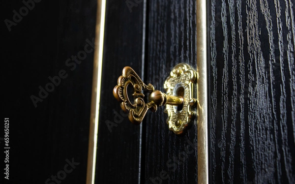 Fototapeta Key is in the keyhole of an antique cabinet door. Closed mysterious door with an old key.
