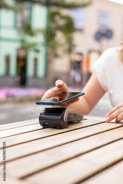 Obraz Close up from hands of young woman paying with her smart phone, NFC technology concept