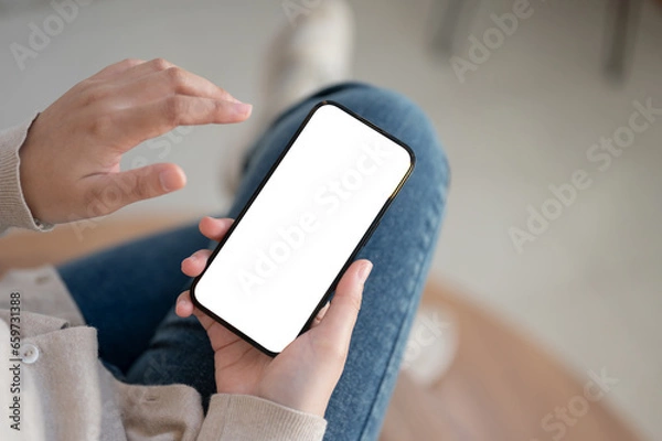Fototapeta Top view image of a white-screen smartphone mockup is in a woman's hands.
