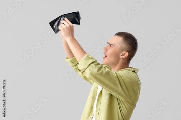 Fototapeta Shocked young man with empty wallet on light background