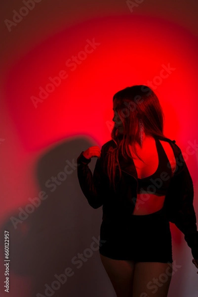 Fototapeta Beautiful young model wearing black clothes posing for photo illuminated in red color.