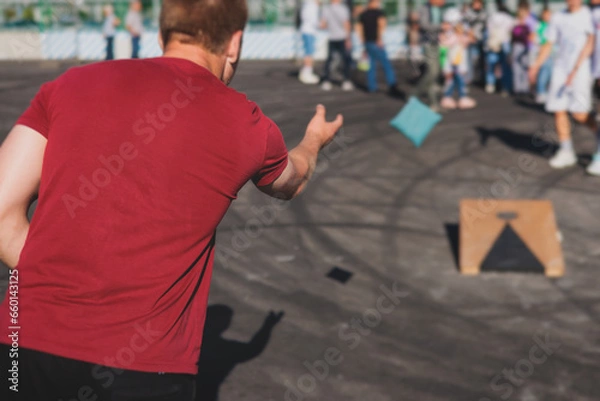 Fototapeta Cornhole game set, process of throwing bean bags, kids children tossing bean sacks, corn hole  in the backyard, wooden boards for corn-hole tournament in the summer sunny day