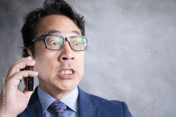 Fototapeta スマホで通話する男性　内容を聞いてびっくりする驚愕の表情のアップ　投資失敗など