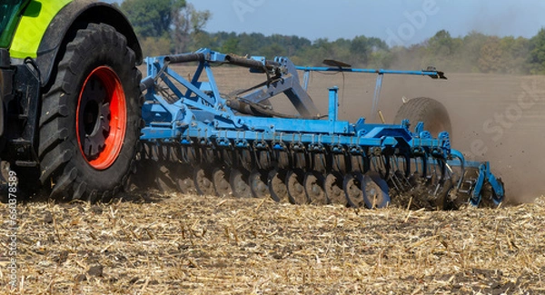 Fototapeta The tractor works in the field with a plow with a disc harrow. Seasonal tillage for subsequent sowing of grain. Photo series