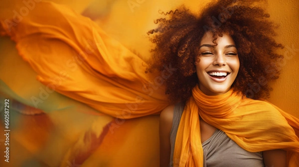 Fototapeta A beautiful, smiling African-American woman with wildly curly afro hair and a long scarf around her neck, billowing in the wind around her in autumn colors.