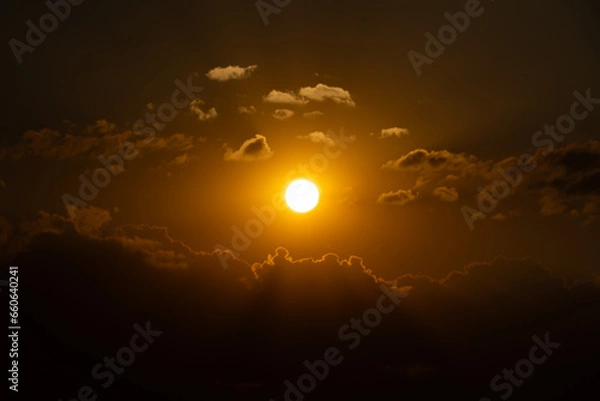 Obraz The sun setting among the clouds. Orange saturated sunset. Sun rays reflecting from delicate clouds.