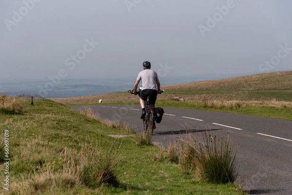 Obraz Dartmoor, Devon, Englaand, UK. 04.09.2023.  Man cycling on  an empty road  in Dartmoor national park in Devon, UK