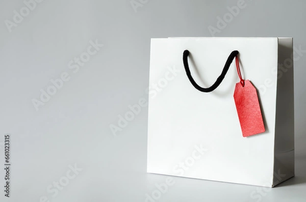 Fototapeta White shopping paper bag with red blank price tag on white background for Black Friday shopping sale concept.