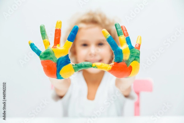 Fototapeta little blonde girl shows her hands painted with multi-colored paint on a white background.