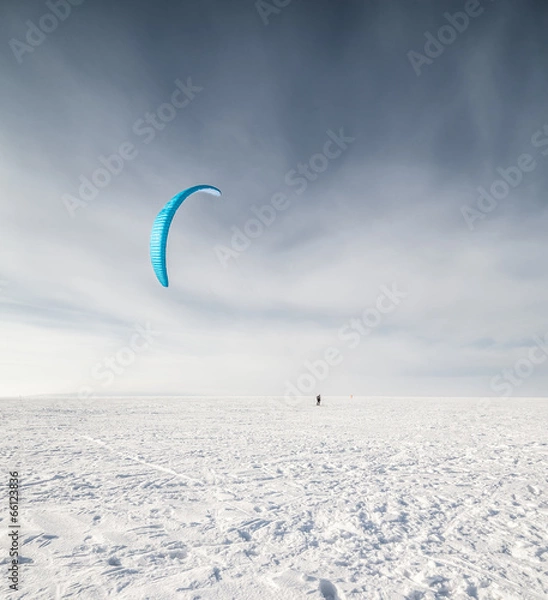 Fototapeta Kiteboarder with blue kite on the snow
