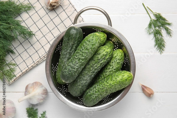 Fototapeta Colander with fresh cucumbers, garlic and dill on white wooden background