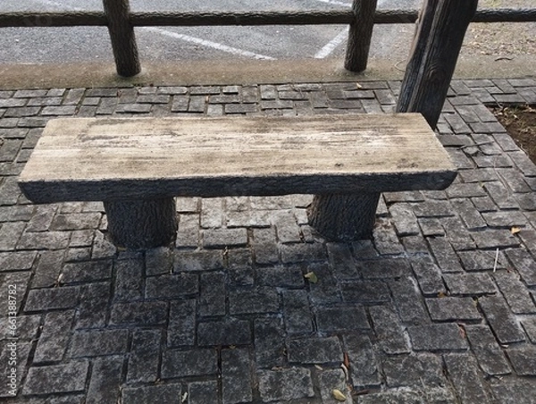 Obraz 石畳のエリアに木目調の石の椅子が設置されている。