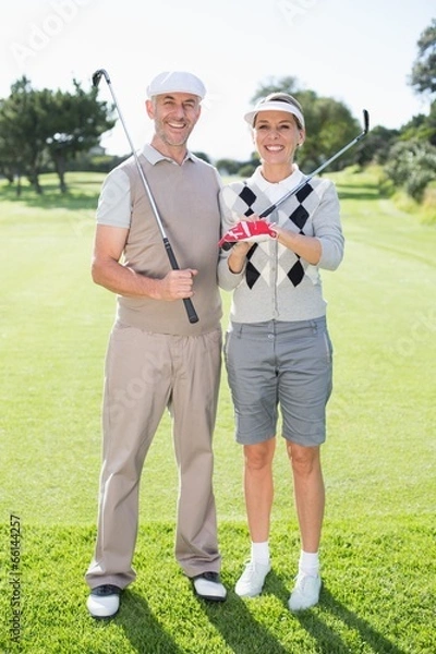 Fototapeta Golfing couple smiling at camera holding clubs